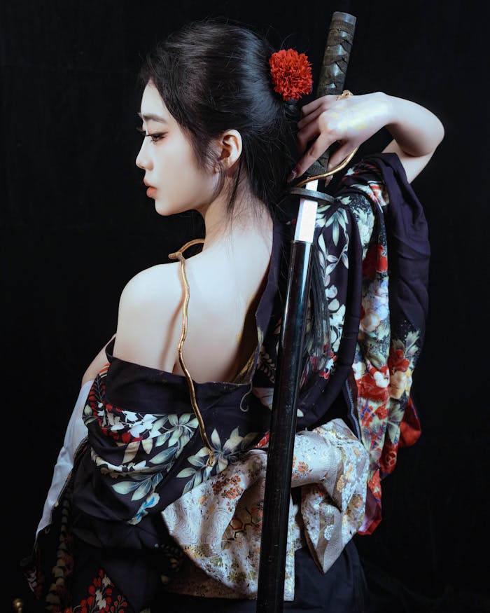 Portrait of a woman in a floral kimono holding a katana with a red flower hair accessory.